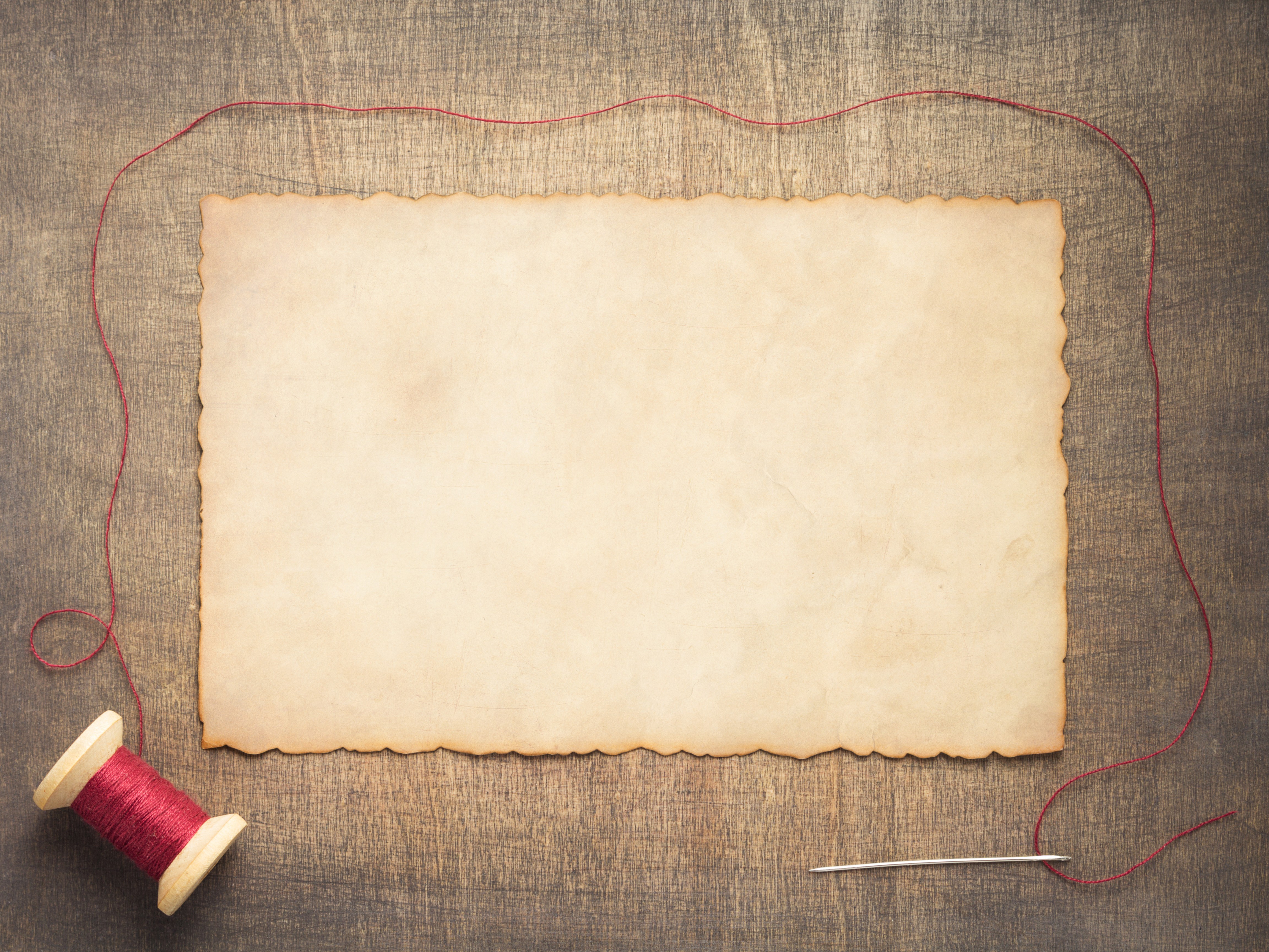 A spool of red thread next to a blank piece of parchment.