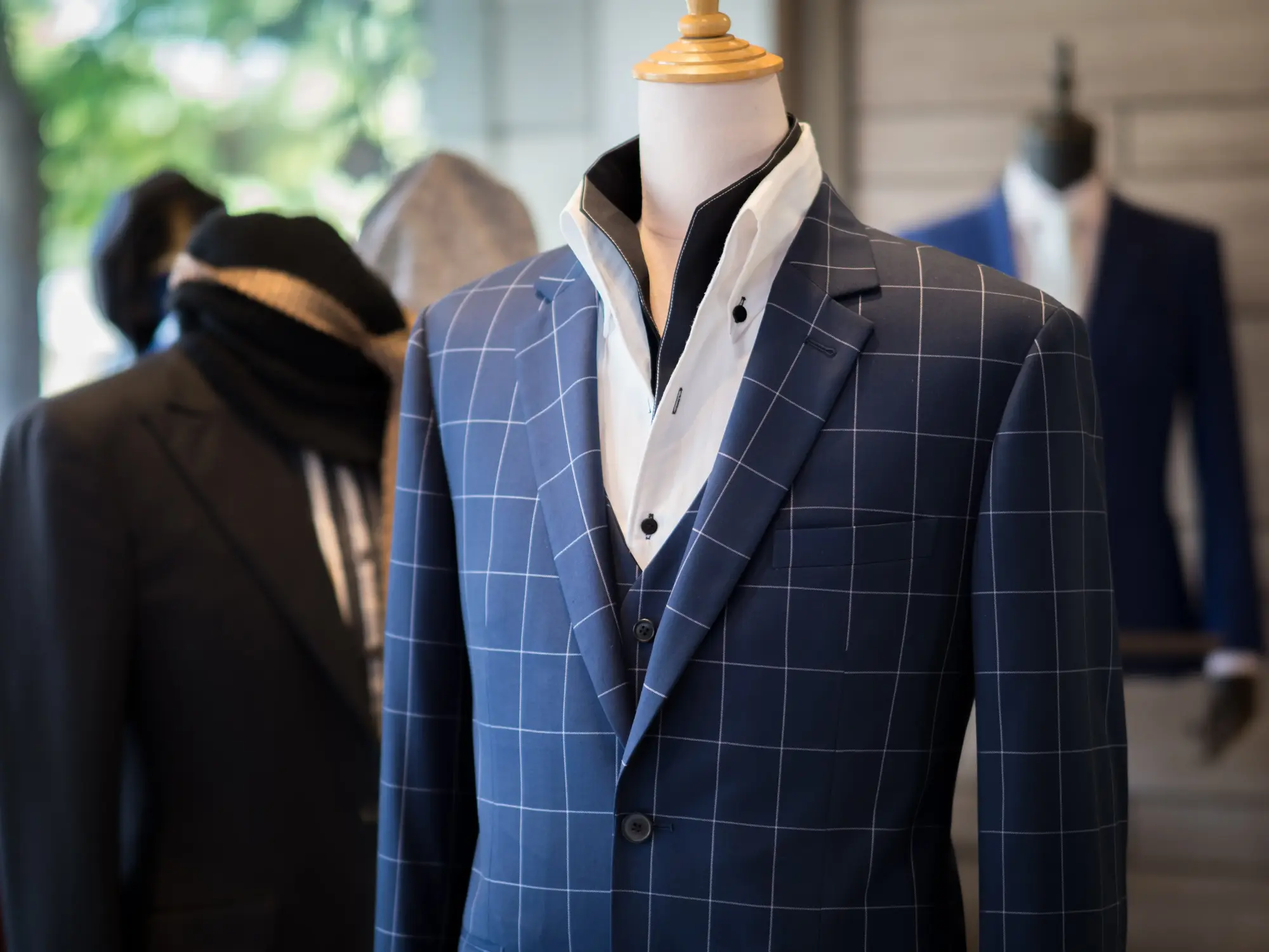 Blue windowpane three piece suit displayed on a tailor’s mannequin, with a white shirt and contrasting dark collar detail.