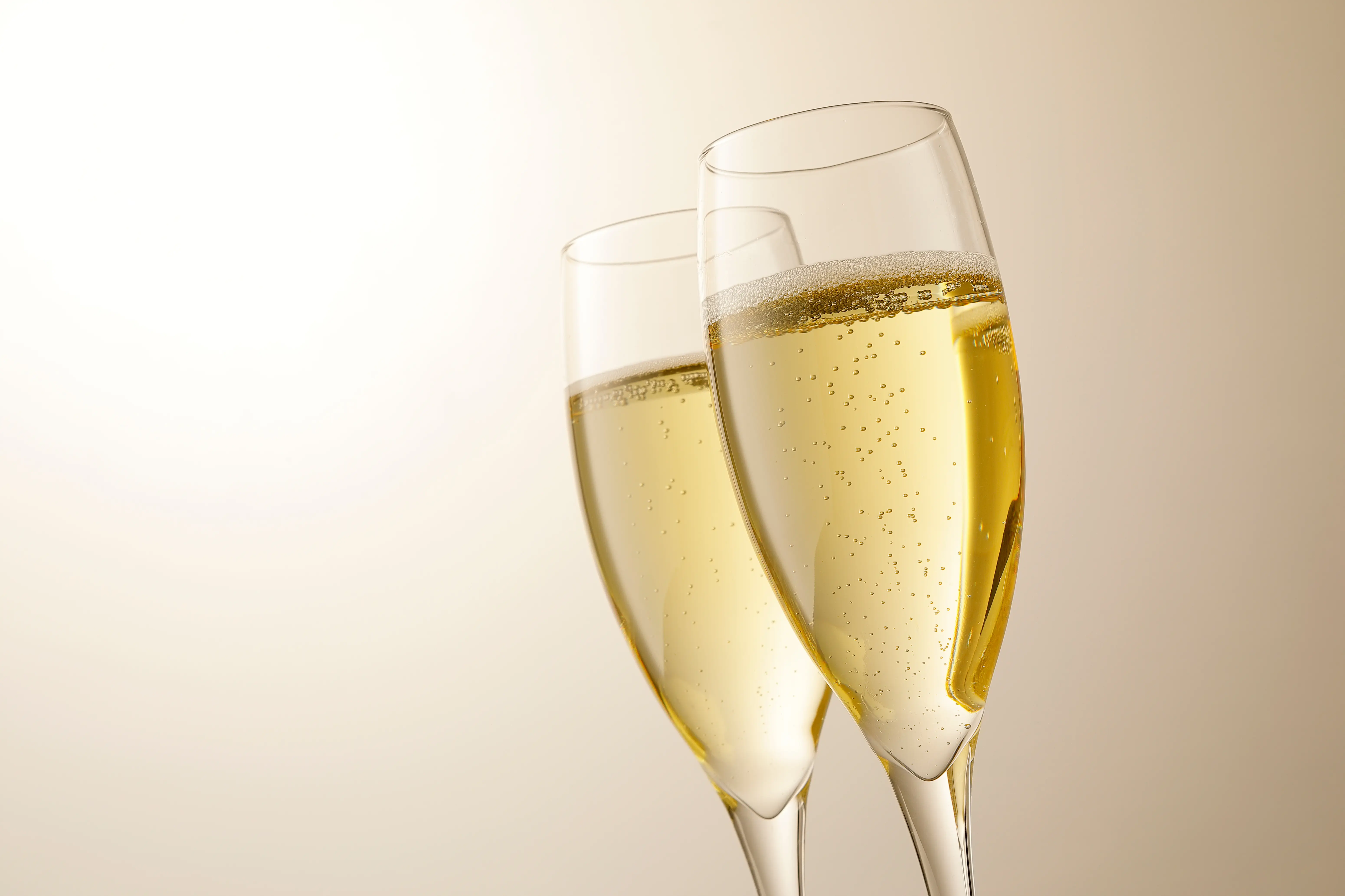 Two champagne flute glasses filled with sparkling wine against a creamy-golden background